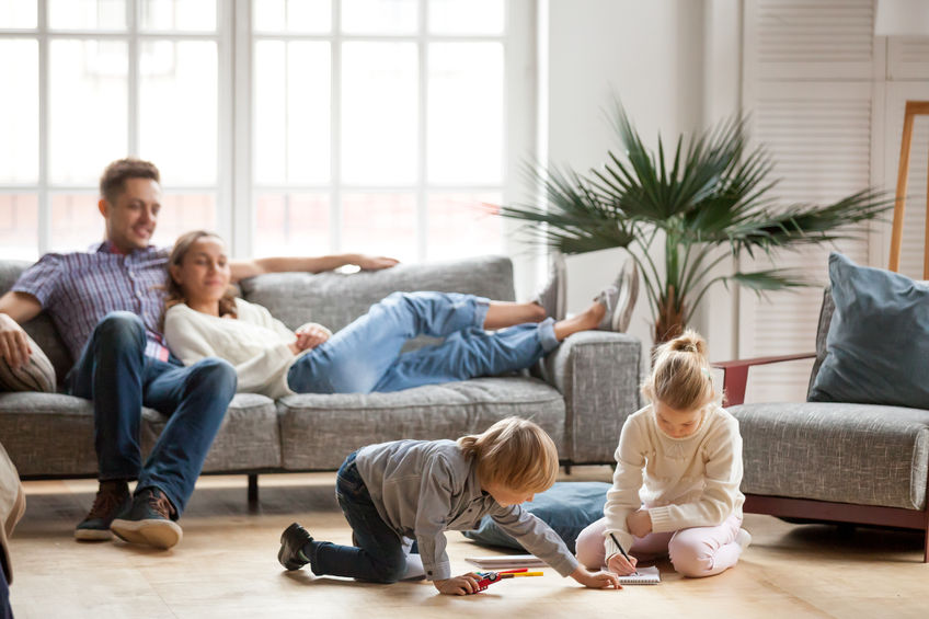 Children siblings playing drawing together while parents relaxin Children sister and brother playing drawing together on floor while young parents relaxing at home on sofa, little boy girl having fun, friendship between siblings, family leisure time in living room